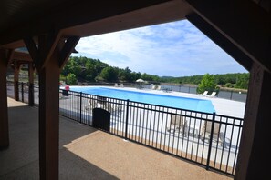 A view of a swimming pool with a black fence, lounge chairs, and a covered area with wooden beams. - StoneBridge Resort (Branson West)