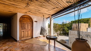 Habitación amplia con puerta de madera, un sillón colgante y un ventanal con vistas al exterior.