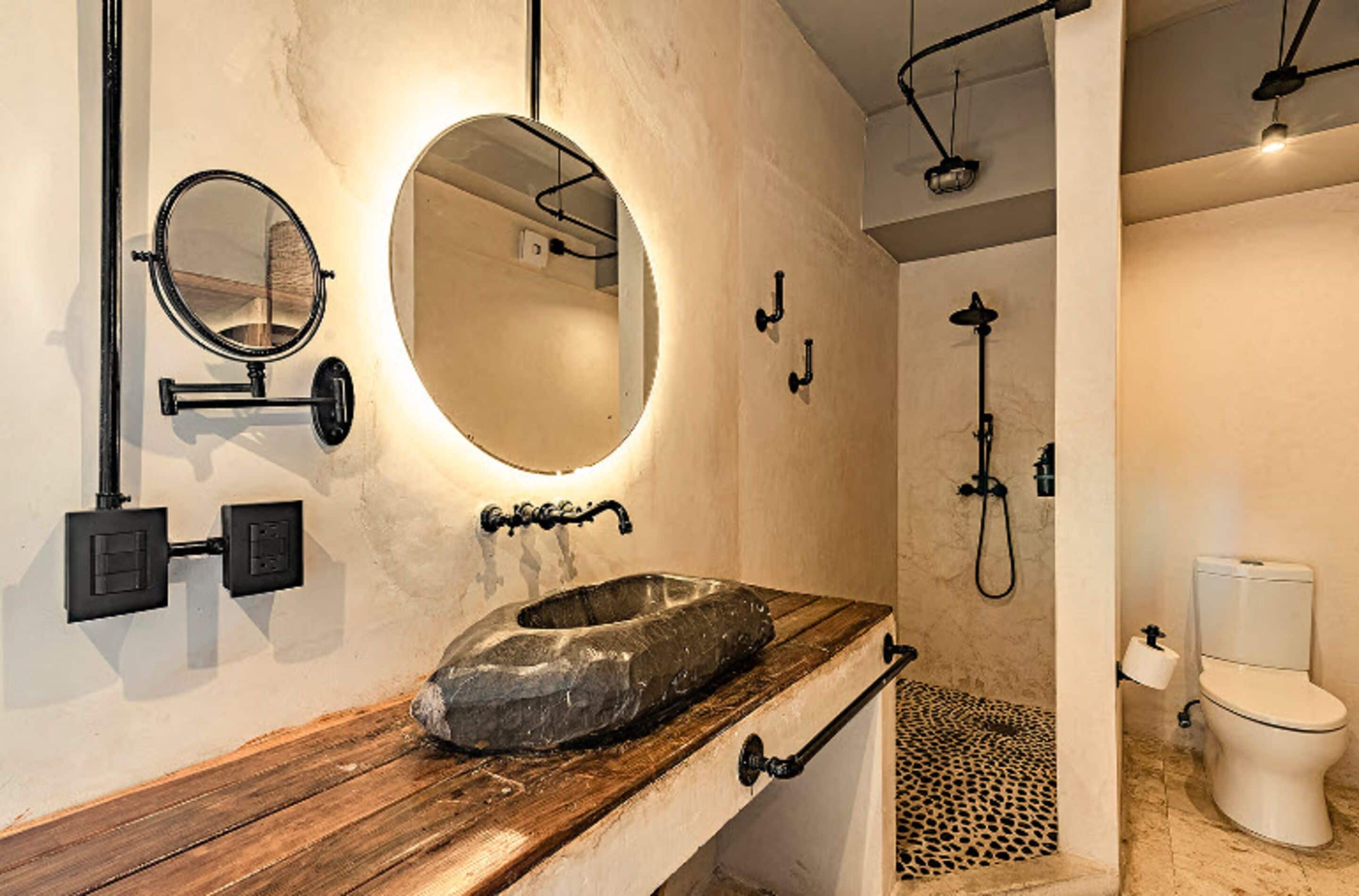 Un baño con tocador de madera, lavamanos de piedra, espejo redondo y ducha con piso estampado de leopardo.