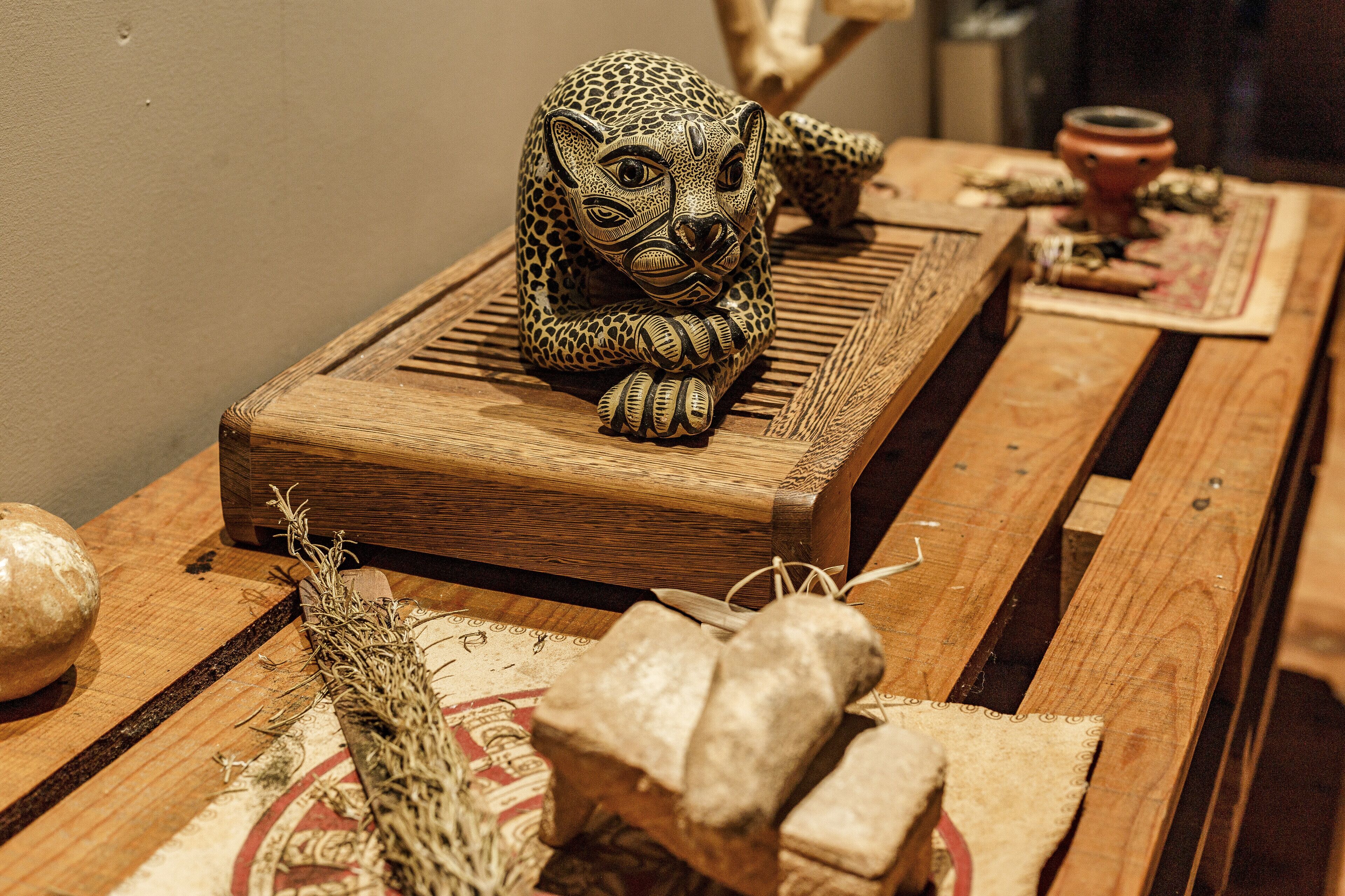 Ein Holztisch mit einer geschnitzten Holzskulptur eines Leoparden, einer kleinen Schale und getrockneten Kräutern.