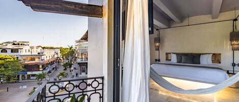 A balcony with a view of a street, a bed with a hammock, and a potted plant.