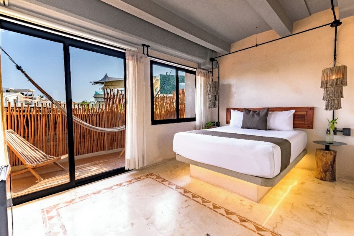 A bedroom with a large bed, a view of a wooden fence and a pagoda, and a hammock outside.