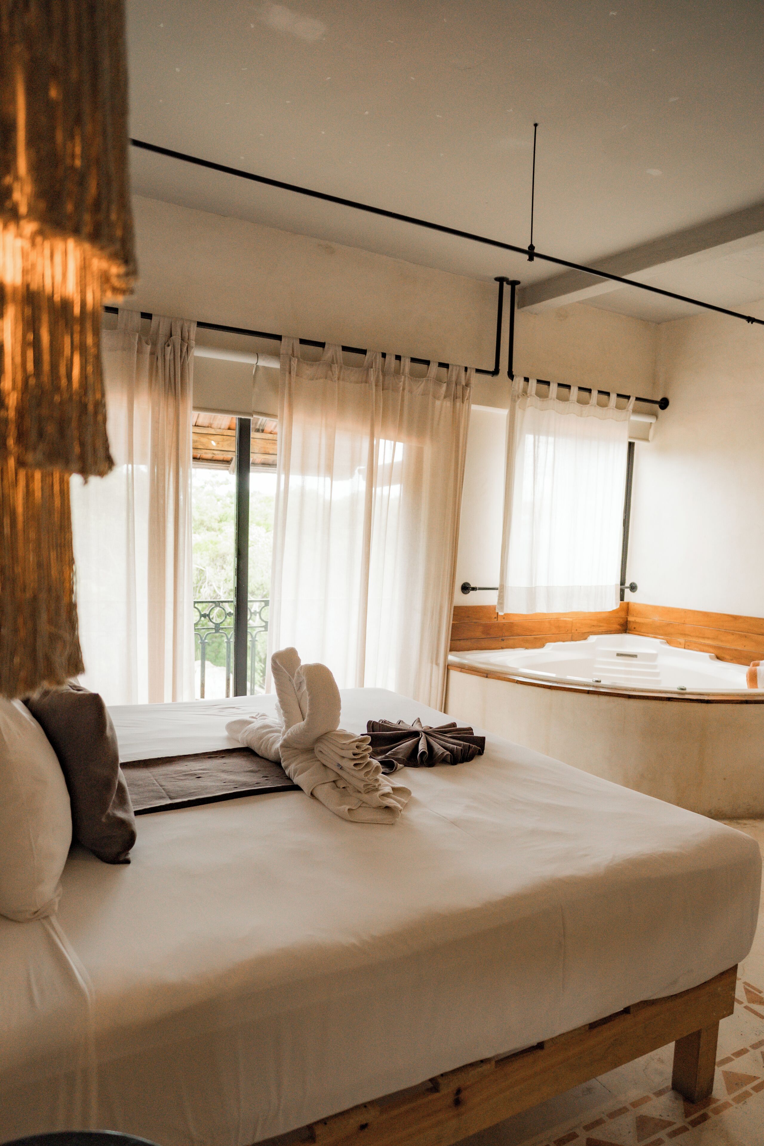 Ein Schlafzimmer mit einem Bett, einem Holz-Kopfteil, einem Fenster mit Vorhängen und Blick ins Grüne.