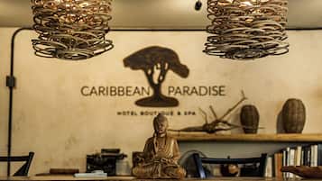 Una estatua de Buda en posición meditativa sobre una mesa de madera en una habitación con un letrero que dice 'Caribbean Paradise Hotel Boutique & Spa'.