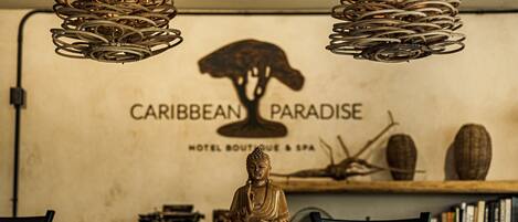 Una estatua de Buda en posición meditativa sobre una mesa de madera en una habitación con un letrero que dice 'Caribbean Paradise Hotel Boutique & Spa'.