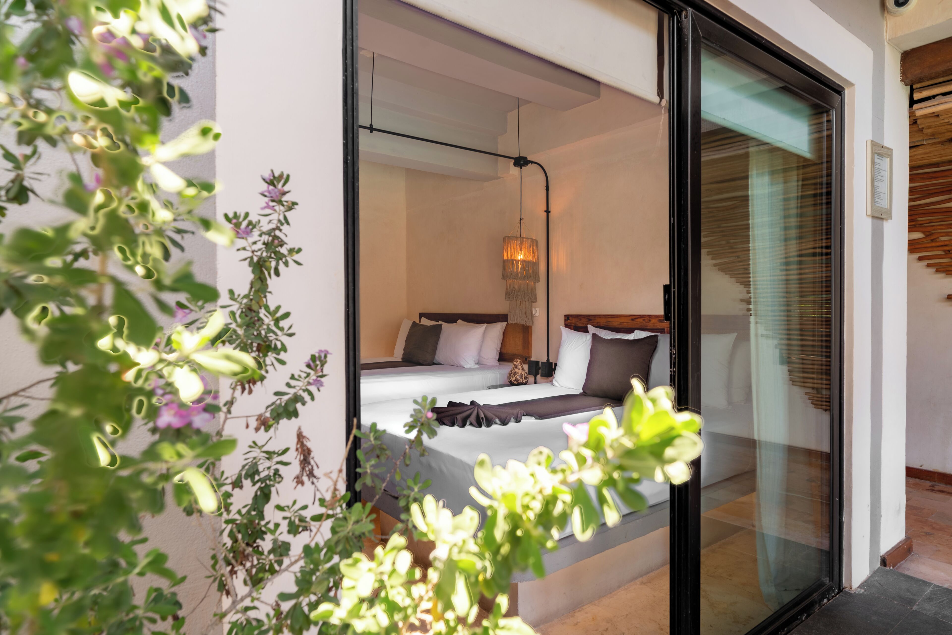 A modern bedroom with a large bed, a hanging light fixture, and a view through a glass door.