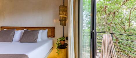 Un dormitorio con una cama, un lámpara colgante, una planta en maceta y un balcón con una silla de madera.