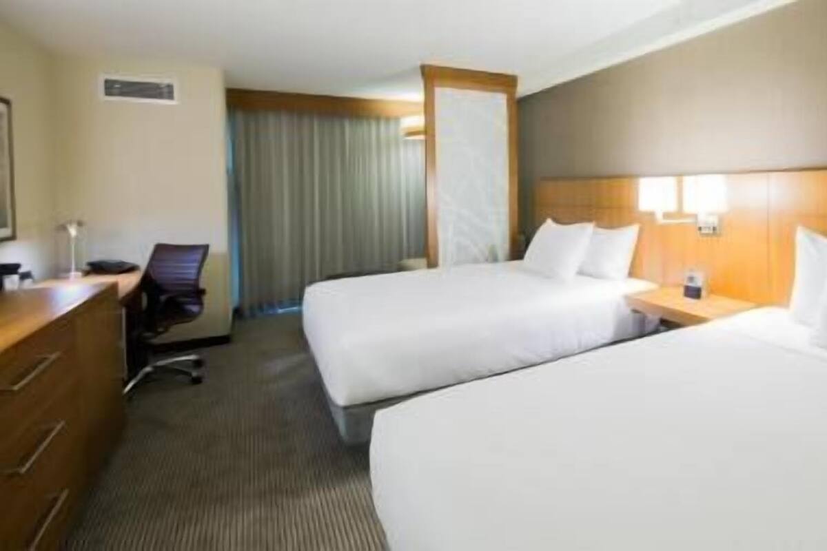 Een hotelkamer met twee bedden, een bureau, een stoel, een nachtkastje en een raam met gordijnen.