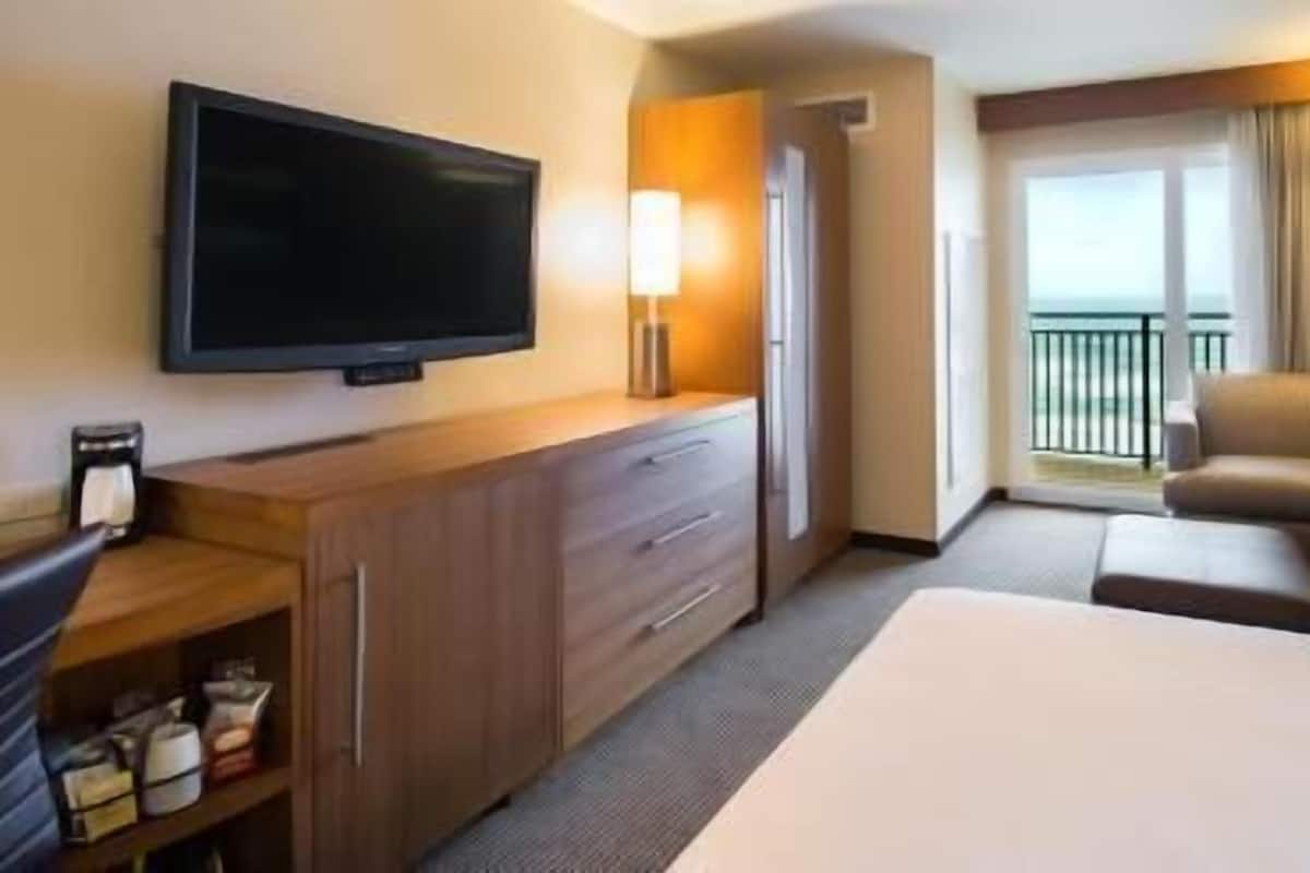 Een hotelkamer met een bed, een televisie, een bureau met een koffiezetapparaat, een bank en een balkon met uitzicht.