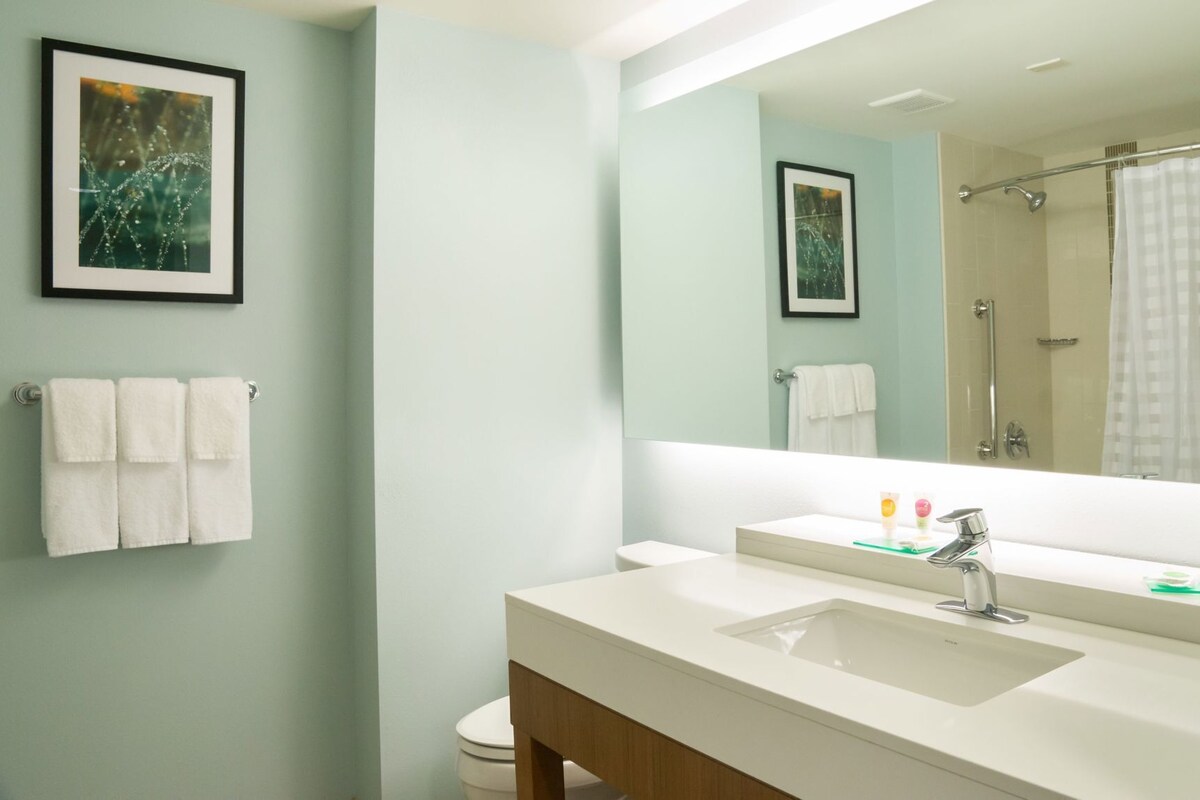 A modern bathroom with a large mirror, white sink, and a shower area.