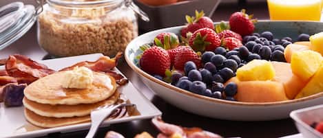 A breakfast spread with pancakes, bacon, eggs, and various fruits.