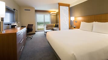 Een hotelkamer met een groot bed, een bureau met lamp, een stoel, een televisie en uitzicht op de omgeving via een schuifdeur.