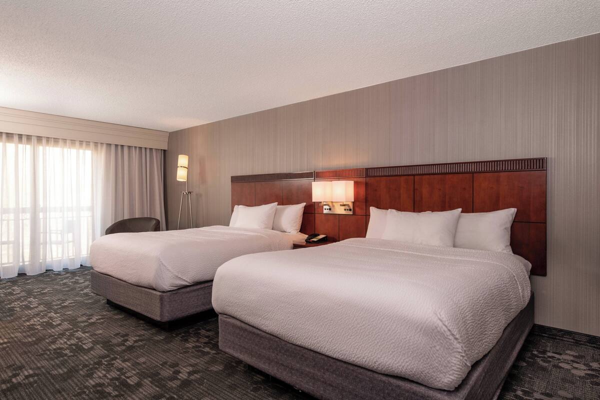 Een hotelkamer met twee bedden, een bureau, een stoel en een groot raam met gordijnen.