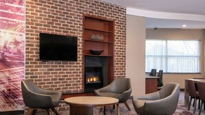 A hotel room with a brick wall, a flat-screen TV, a fireplace, and a seating area with chairs and a table.