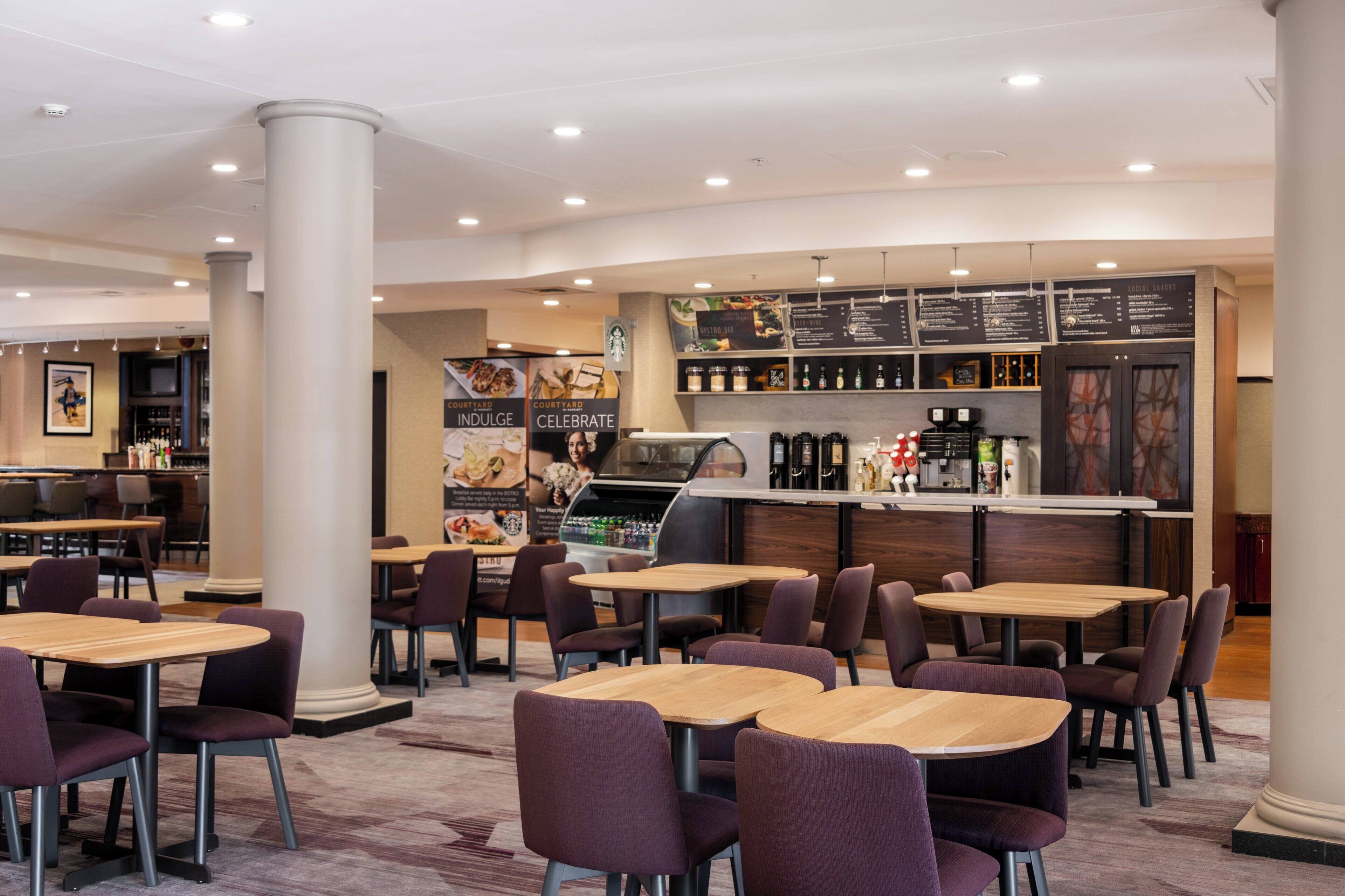 A modern restaurant with round tables and purple chairs, a bar area with a menu, and a coffee machine.