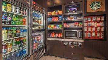 A beverage refrigerator stocked with various drinks, a microwave, and a display of snacks and coffee products.