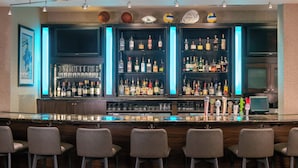 A bar area with multiple shelves of bottles, a flat-screen TV, and bar stools.
