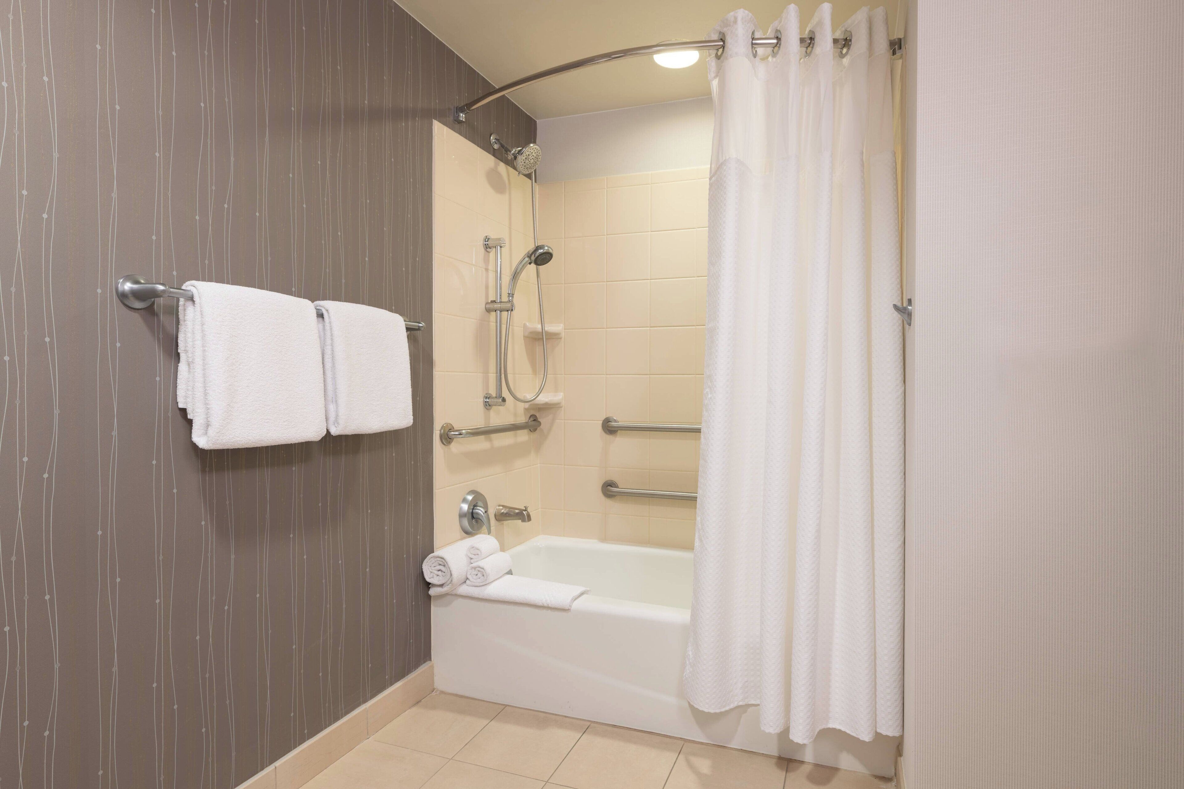 A bathroom with a bathtub, shower, and toilet. There are two towels hanging on the wall.