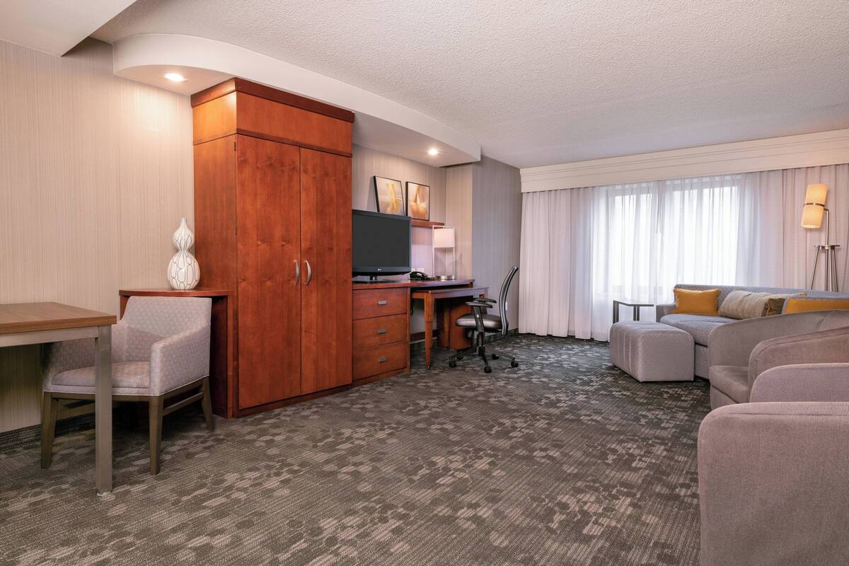 Een hotelkamer met een houten garderobe, een bureau met een televisie, een bank en een stoel.