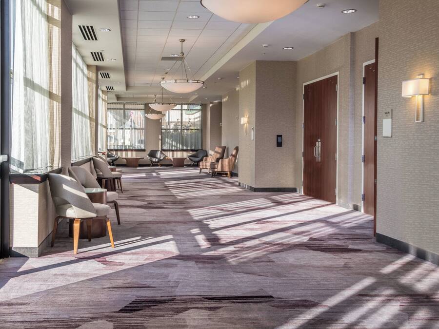 Un couloir d’hôtel avec des sièges, de grandes fenêtres et une moquette à motifs.
