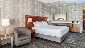 A hotel room with a large bed, a chair, a desk, and a vanity with a mirror.