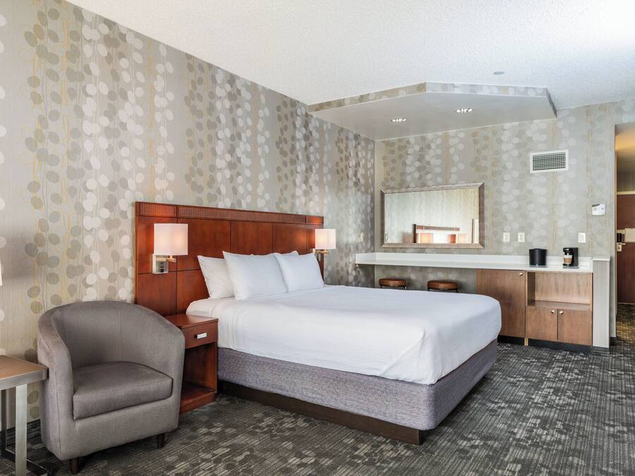 A hotel room with a large bed, a chair, a desk, and a vanity with a mirror.