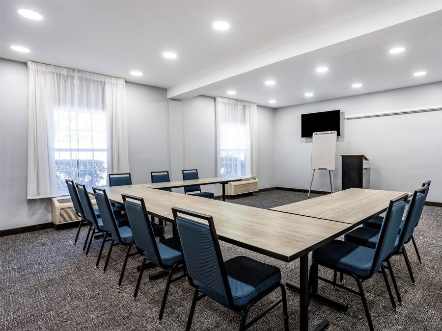Una sala de conferencias con una larga mesa, sillas azules, una pantalla de proyector y una pizarra.