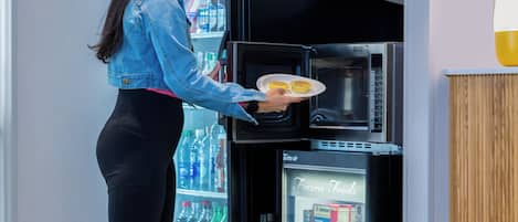 A woman retrieving a plate of food from a black refrigerator in a commercial setting.