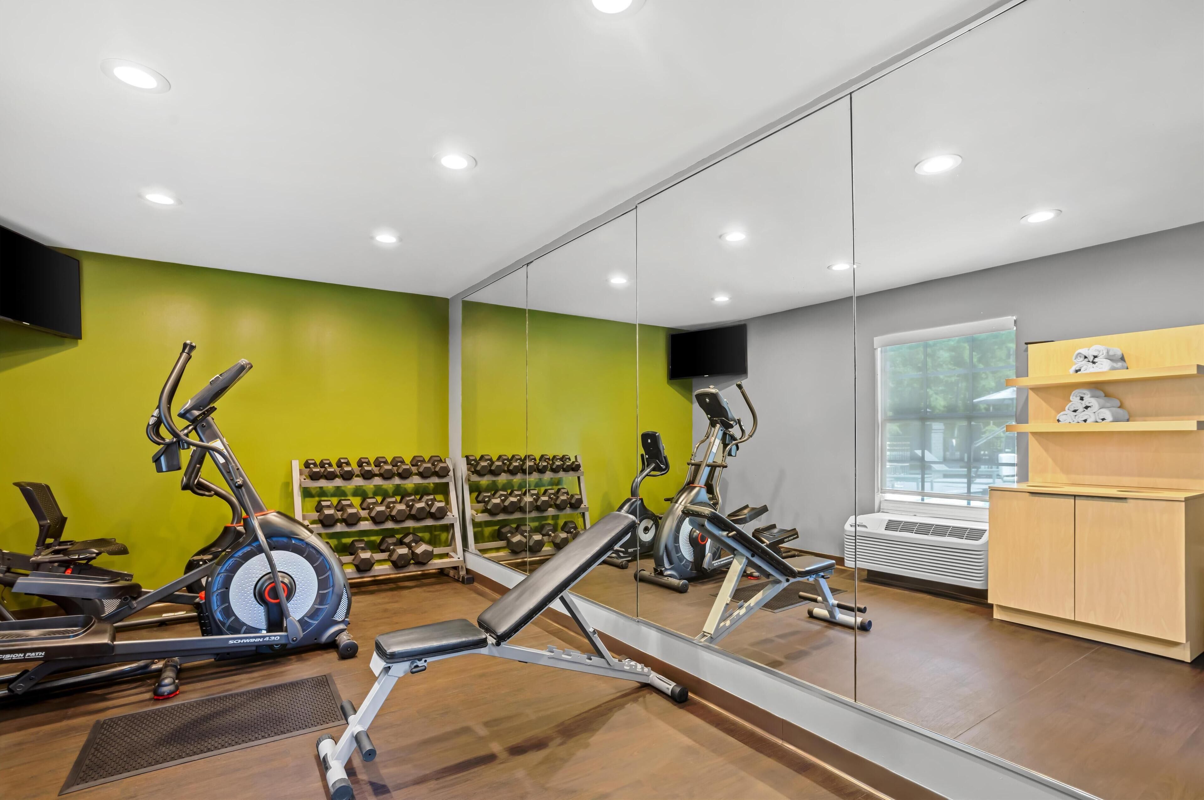 Un gimnasio con equipo de ejercicio, un espejo y un televisor instalado en la pared.