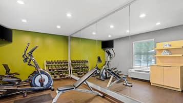 Un gimnasio con equipo de ejercicio, un espejo y un televisor instalado en la pared.