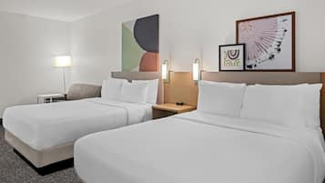 Habitación de hotel con dos camas, una mesita de noche, una lámpara y dos luces empotradas en la pared.
