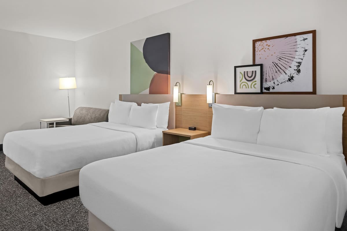 Habitación de hotel con dos camas, una mesita de noche, una lámpara y dos luces empotradas en la pared.