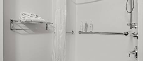 A bathroom with a shower, a towel rack with folded towels, and a shelf with toiletries.
