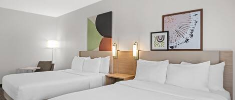 A hotel room with two beds, a nightstand, a lamp, and abstract wall art.