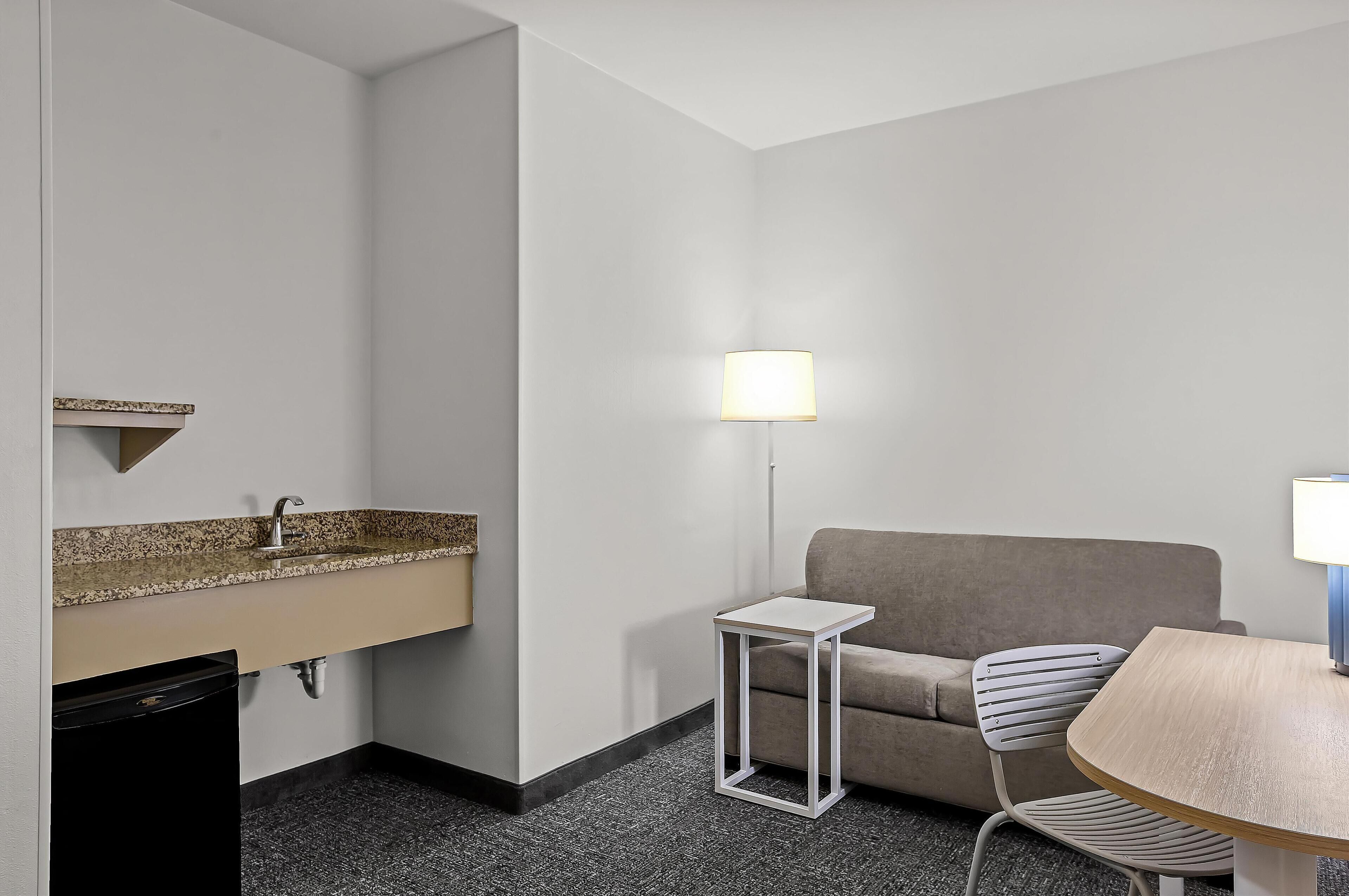 Ein Hotelzimmer mit Küchenzeile, einer Couch, einem Esstisch und einer Lampe.