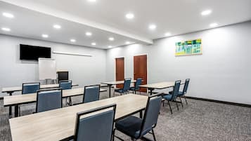 Una sala de conferencias con varias mesas y sillas, un televisor de pantalla plana montado en la pared y piso alfombrado.