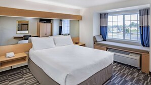 A hotel room with a large bed, a desk, a chair, a TV, a window with curtains, and a mirror.