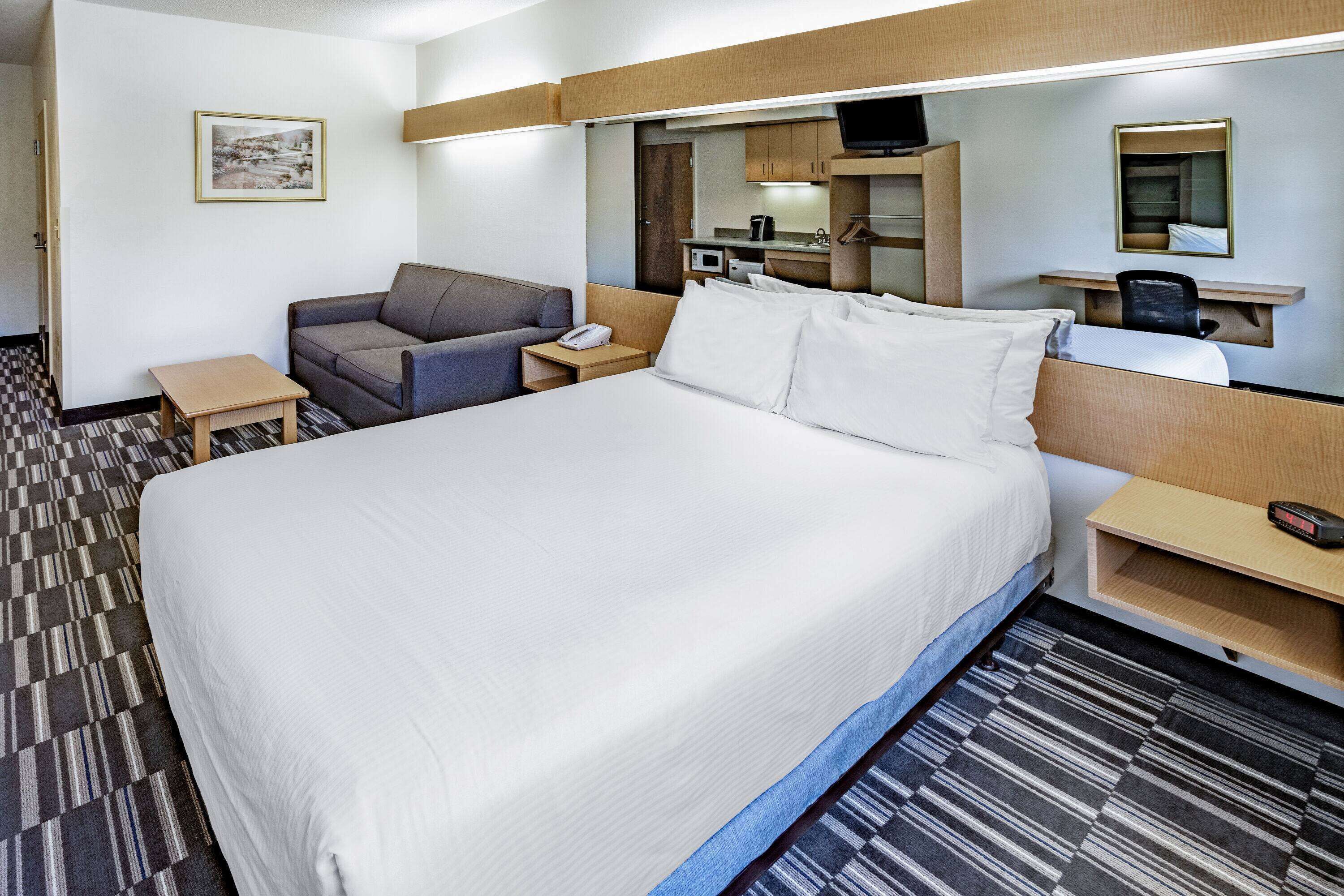 Habitación de hotel con una cama grande, un sofá, un escritorio con computadora, una mesita y un televisor.