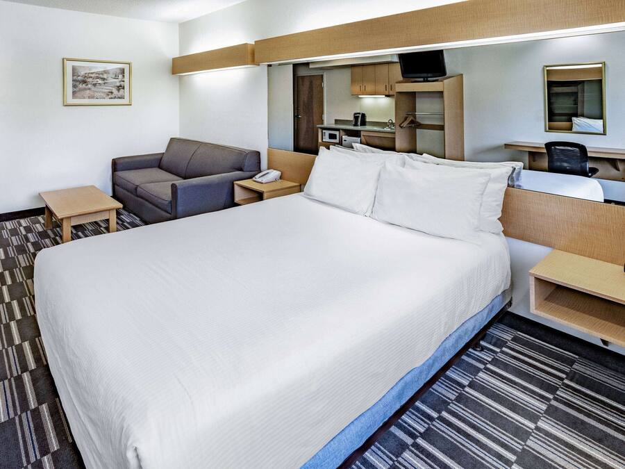 Habitación de hotel con una cama grande, un sofá, un escritorio con computadora, una mesita y un televisor.