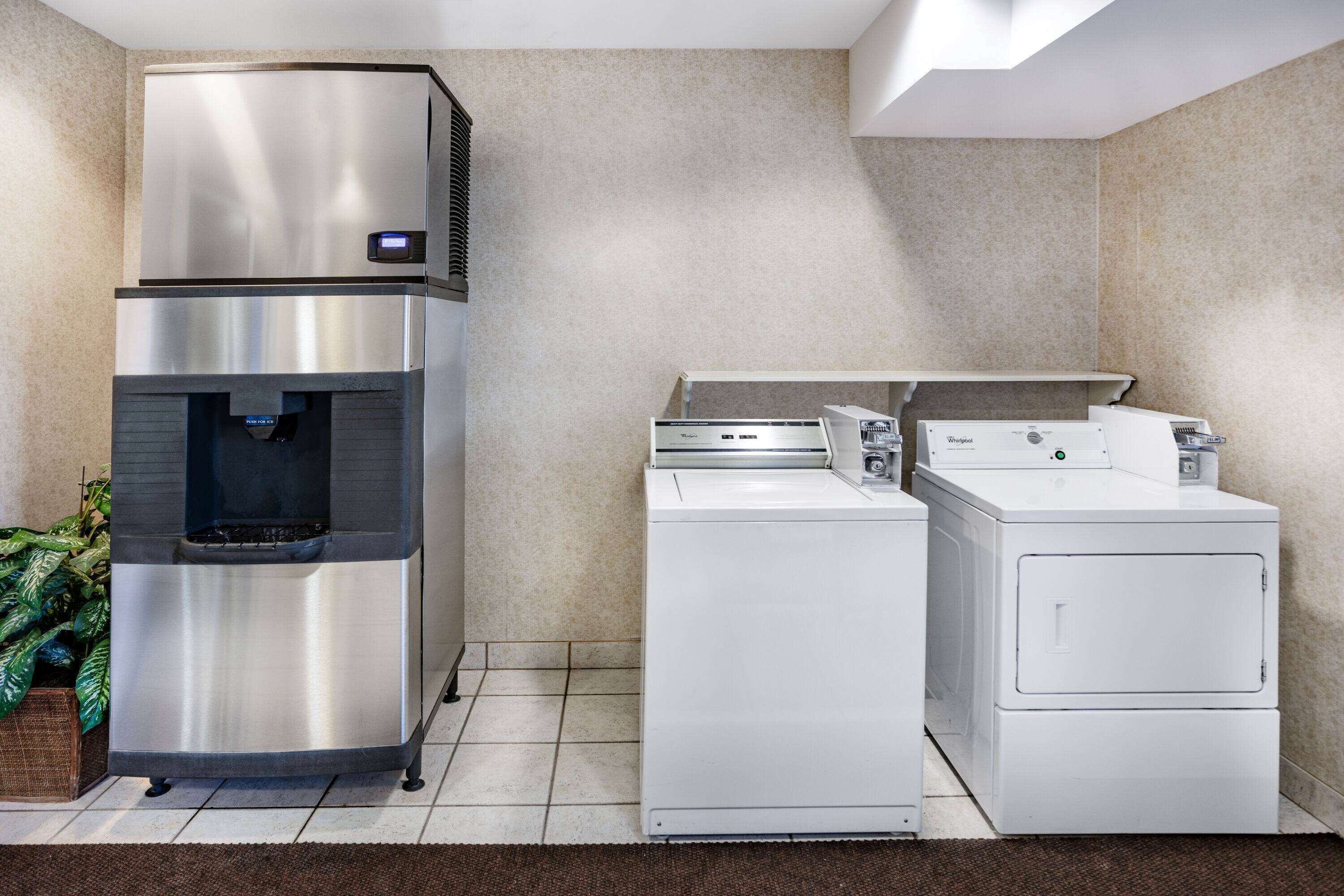 Cocina compacta con refrigerador de acero inoxidable, dispensador de agua integrado y lavadora y secadora de carga frontal.