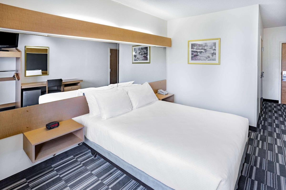 A hotel room with a bed, a desk, a chair, a mirror, and a telephone.