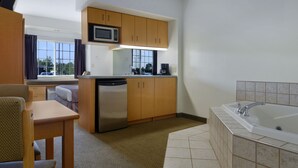 A compact hotel room with a kitchenette, a sink, a microwave, a dishwasher, a seating area, and a bathtub.