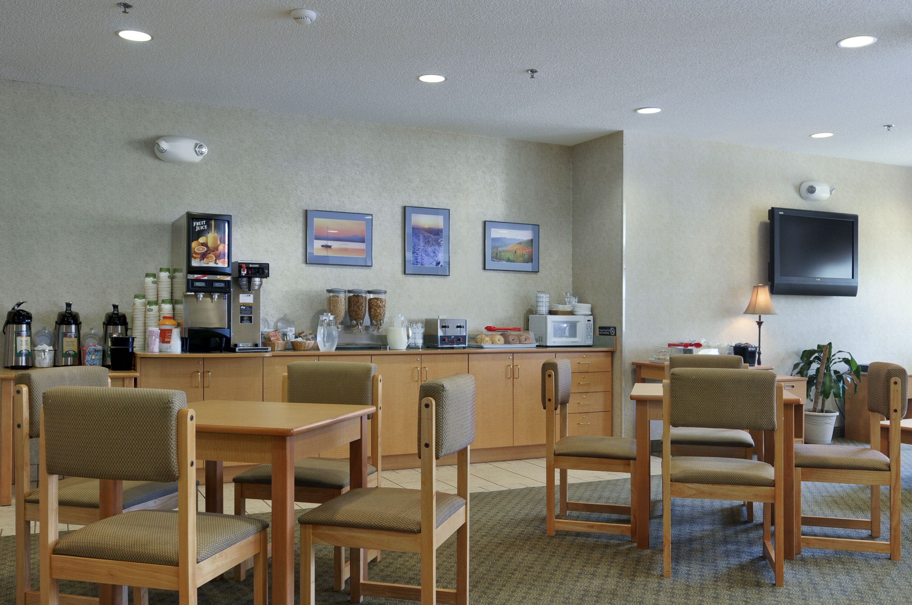 A hotel lobby with wooden furniture, a coffee station, and framed pictures on the wall.