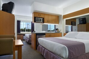 A compact hotel room with a bed, a desk, a microwave, a television, and a window with curtains. - Microtel Inn & Suites by Wyndham Plattsburgh (Plattsburgh)
