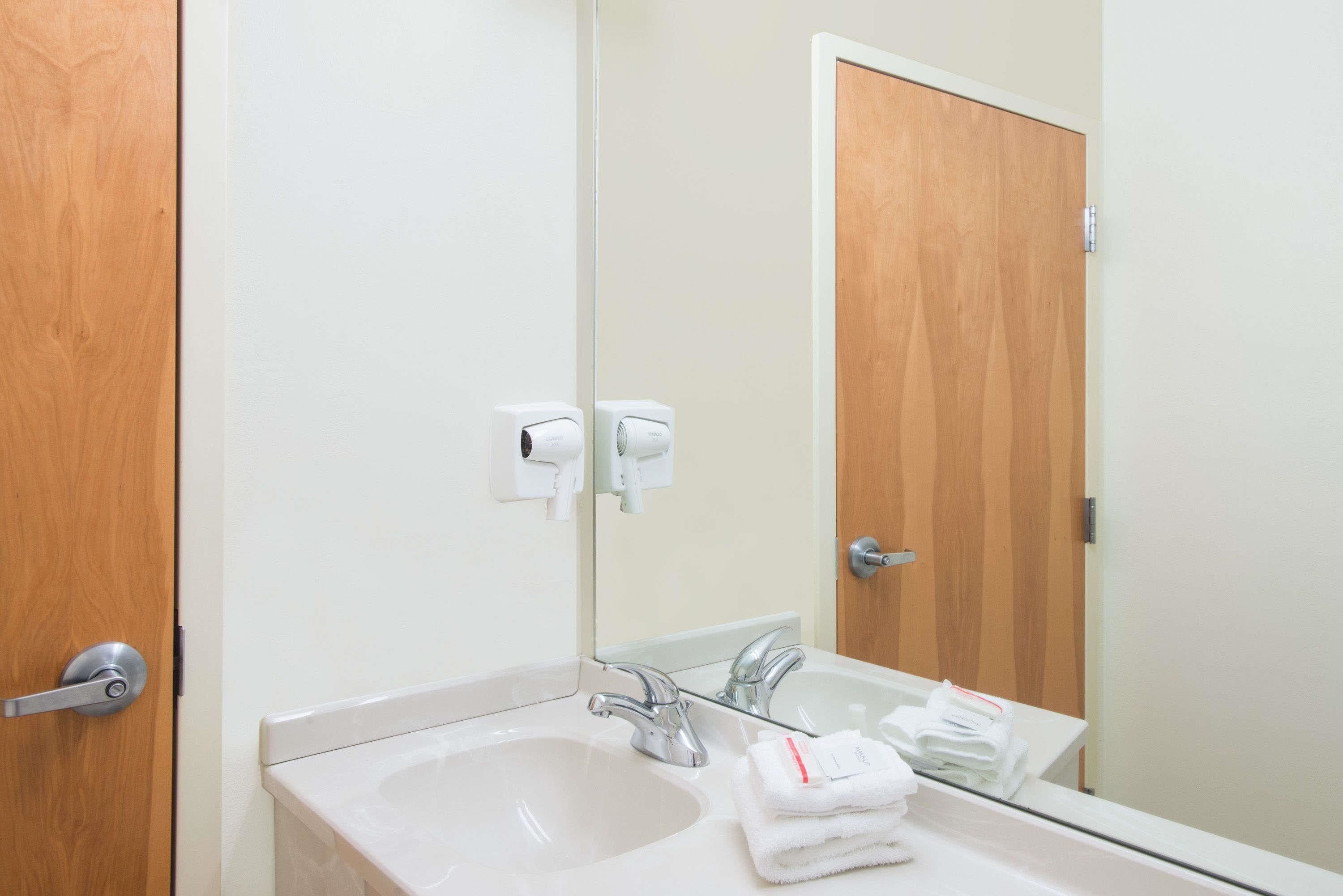 A bathroom with a sink, mirror, and towel dispenser.