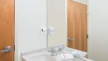 A bathroom with a sink, mirror, and towel dispenser.