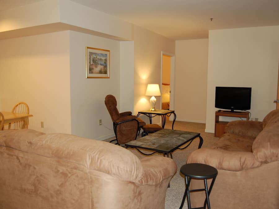 A living room with beige sofas, a wooden coffee table, a TV stand, and a lamp.