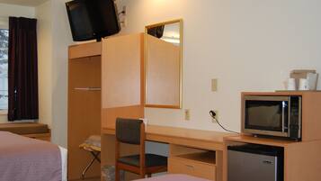 Een hotelkamer met een bed, een bureau met stoel, een aan de muur bevestigde televisie, een magnetron en een koelkast.