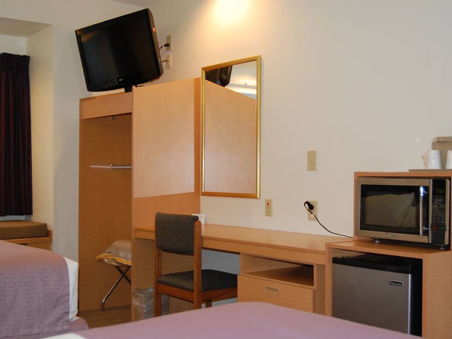 A hotel room with a bed, a desk with a chair, a television mounted on the wall, a microwave, and a refrigerator.