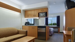 A compact hotel room with a kitchenette, a sofa, a small dining table, and a view of the outdoors.